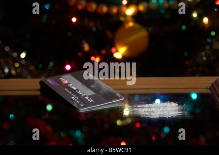 Carte de crédit platine avec des lignes de cocaïne simulée sur un miroir en face de l'arbre de Noël Banque D'Images