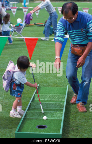 Young Asian Girl playing Miniature Golf et aidé par son père Banque D'Images