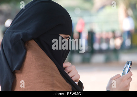 Une femme égyptienne portant un vêtement traditionnel Niqab noir en utilisant un téléphone cellulaire en Egypte Banque D'Images