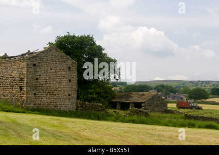 Vue à travers champs - une ancienne grange dans l'avant-plan et d'un tracteur travaillant aux côtés d'une ensileuse, dans l'arrière-plan Banque D'Images