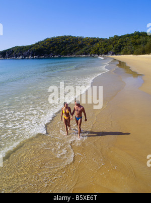 Vue aérienne d'un jeune couple tenant la main tout en marchant le long d'une plage ensoleillée avec des eaux claires Banque D'Images