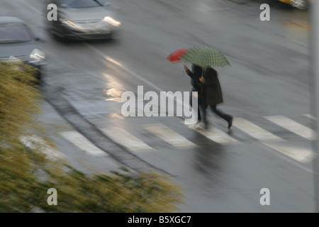 Deux personnes avec parasols colorés dans la pluie en ville Banque D'Images