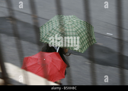 Deux personnes avec parasols colorés dans la pluie en ville Banque D'Images