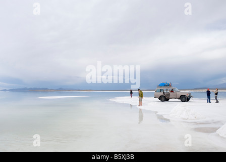 Un groupe de touristes se tiennent près de l'eau des plaines de sel de Bolivie Salar de Uyuni Banque D'Images