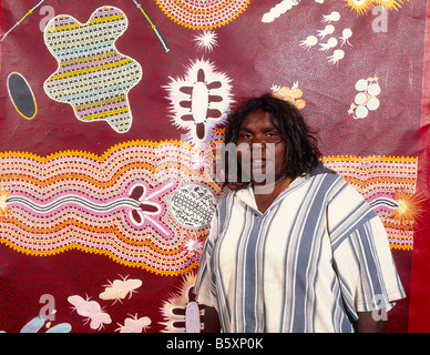 Brenda Nungurrayi Lynch (b1958) artiste debout devant sa peinture d'art aborigène colorée du désert occidental avec des motifs traditionnels Banque D'Images