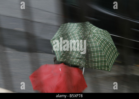 Deux personnes avec parasols colorés dans la pluie en ville Banque D'Images