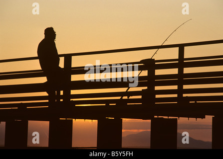 Coucher du soleil avec homme plus âgé qui se profile la pêche au large de pier Marina Shilshole avec montagnes olympiques de l'État de Washington Seattle USA Banque D'Images