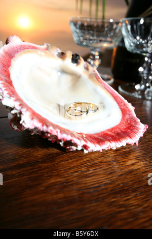 Les anneaux de mariage dans un shell devant un coucher de bouteille de champagne et verres Banque D'Images