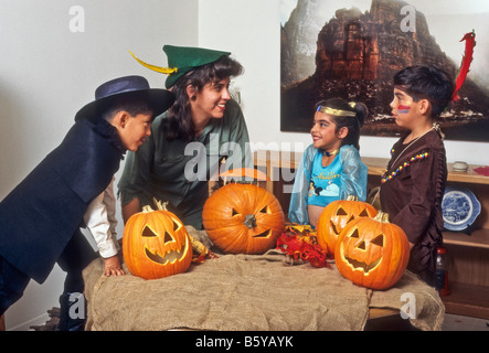 Mère hispanique et trois enfants habillés pour admirer l'Halloween jack-o-lanternes qu'ils ont fait à partir de citrouilles. Banque D'Images