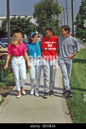 Mixed Race groupe d'adolescents à pied vers le bas sur le trottoir, un garçon portant chemise anti-drogue. Banque D'Images