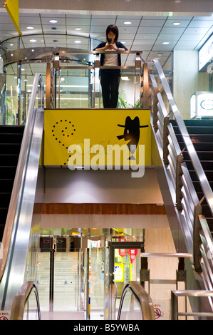 Une femme textos sur son téléphone portable en haut d'un escalator à Shinjuku, Tokyo, Japon. Banque D'Images