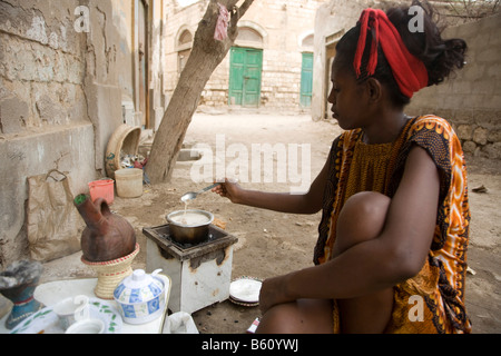Jeune femme, 20-25 ans, la préparation du porridge pour son bébé sur un petit poêle à charbon, de la mer Rouge, Massaoua, l'Erythrée, l'Afrique Banque D'Images