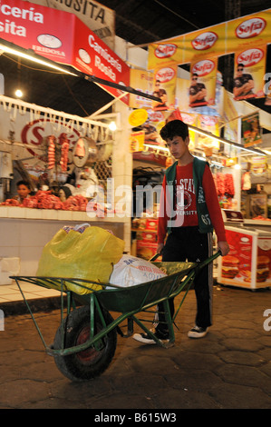 Le travail des enfants, le transport des achats des clients de garçon à l'aide d'une brouette sur le marché local, Santa Cruz, Bolivie, Amérique du Sud Banque D'Images