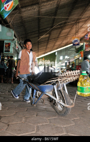 Le travail des enfants, le transport des achats des clients de garçon à l'aide d'une brouette sur le marché local, Santa Cruz, Bolivie, Amérique du Sud Banque D'Images