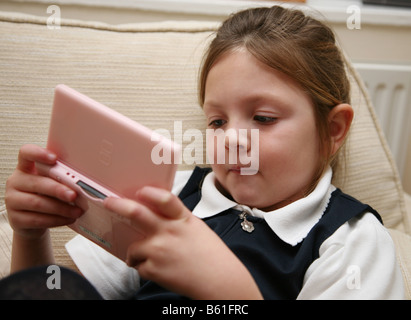 6 ans école fille couchée sur le canapé à jouer sa Nintendo DS Banque D'Images