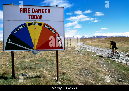 Mountainbiker équitation passé un signe de danger d'incendie, Lindis Pass, île du Sud, Nouvelle-Zélande Banque D'Images