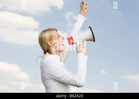 Jeune femme blonde crier dans un mégaphone Banque D'Images