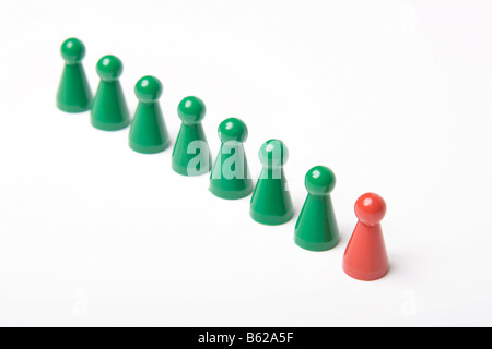 Pièces de jeu Vert debout dans une rangée derrière un seul morceau de jeu rouge, symbolique du leadership Banque D'Images