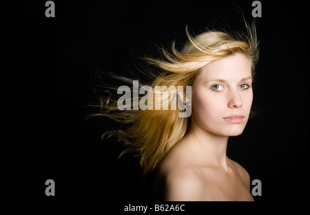 Jeune femme blonde avec de longs cheveux de soufflage in front of black Banque D'Images