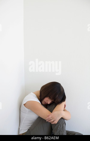 Triste jeune femme assise dans un coin Banque D'Images