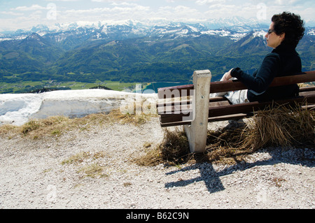 Femme assise sur un banc, profitant de la vue depuis la montagne Schafberg sur le lac Wolfgangsee et les montagnes environnantes, Sal Banque D'Images