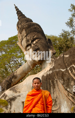 Le moine bouddhiste portant une robe orange en face d'une statue de Bouddha, Bouddha, Parc Suan Xieng Khuan, près de Vientiane, Laos Banque D'Images