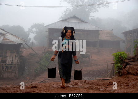 Femme de la tribu Akha Phixo portant des costumes traditionnels portant deux seaux d'eau dans le brouillard dans le village de Ban Mososa Banque D'Images