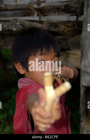 Jeune garçon de la tribu Lao Seng visant au photographe avec sa catapulte dans le village de Ban Tang, province de Phongsali, La Banque D'Images