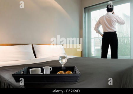 Plateau de petit-déjeuner sur le lit et un homme d'affaires regardant par la fenêtre Banque D'Images