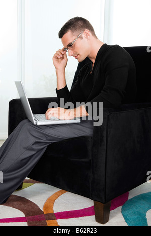 Portrait d'un jeune homme assis dans un fauteuil et de travailler sur un ordinateur portable Banque D'Images