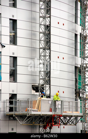 Pause des ouvriers de travailler pendant que sur un échafaudage ledge contre un bâtiment élevé. Banque D'Images