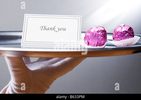 Close-up of a waiter's main portant une plaque avec remerciement et chocolats Banque D'Images