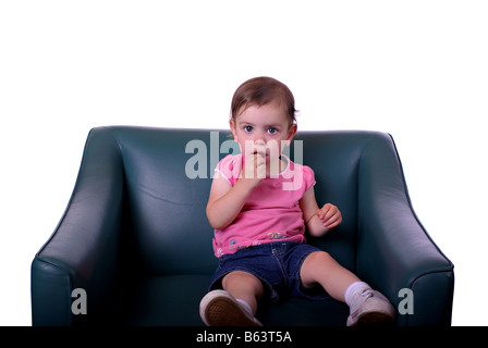 Une petite fille sur un fauteuil en cuir vert en face d'un fond blanc Banque D'Images