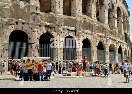 Un commerçant de la rue vendre de fausses marchandises de marque pour les touristes par le Colisée et soldats romains posent pour les touristes, Rome, Latium, Italie. Banque D'Images