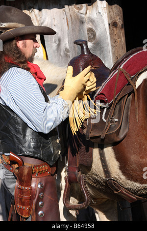 Un cowboy qui décolle ses gants en cuir jaune fringe selle Banque D'Images