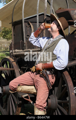 Un vieux cowboy minuterie appuyé contre le chuck wagon en tenant un verre Banque D'Images