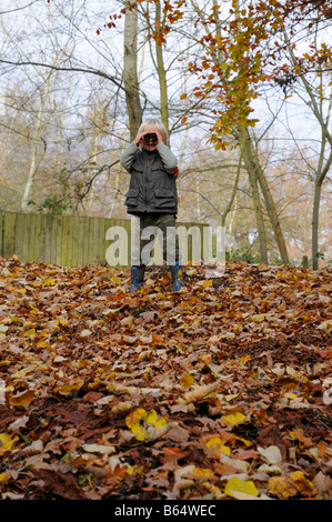 Un jeune garçon jouant de ses pairs par des jumelles dans un bois sur une journée d'automne. Banque D'Images