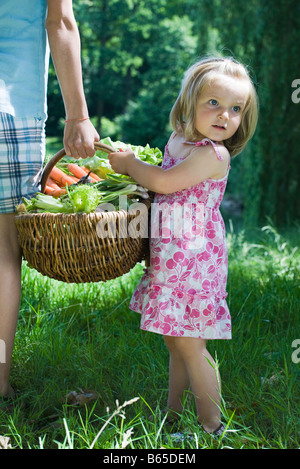 Petite fille debout à côté d'une soeur plus âgé, tenant un grand panier plein de produire, cropped view Banque D'Images