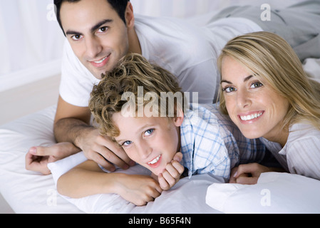 Les parents et le fils lying on bed, smiling at camera, portrait Banque D'Images