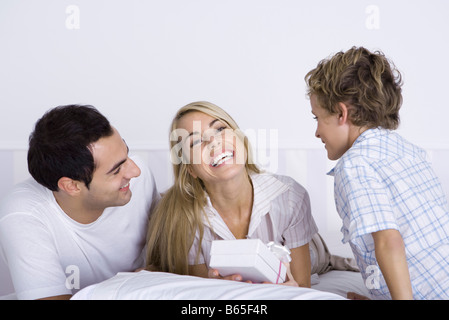 Family Lying in Bed together, woman holding gift and smiling at camera Banque D'Images