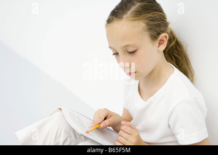 Girl leaning against wall, la lecture, l'ordinateur portable holding pencil Banque D'Images