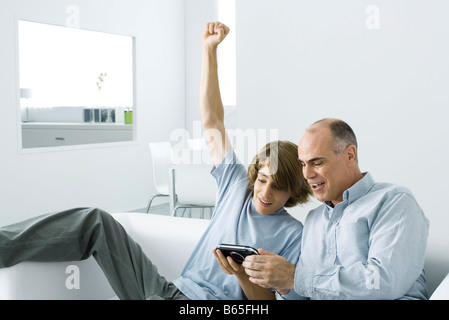 Teen boy showing jeu vidéo de poche à son père, le bras levé Banque D'Images