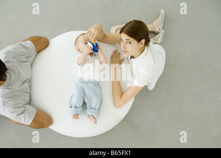 Mère jouer avec bébé couché sur un pouf, père assis avec dos tourné à eux, overhead view