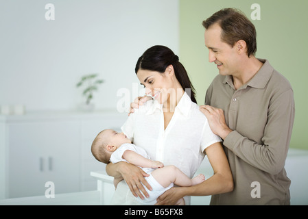 Woman holding baby, l'homme debout derrière, smiling Banque D'Images