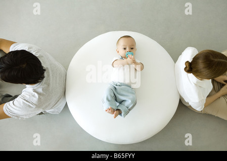 Bébé couché sur un pouf, mère et père assis avec dos tourné, overhead view