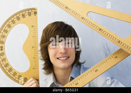 Jeune homme tenant divers instruments de mesure, smiling at camera Banque D'Images