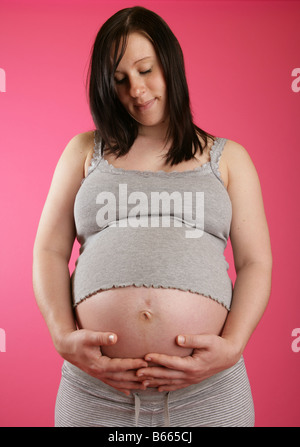 Une vue sur la tête d'un dark haired 38 semaines (9 mois) enceinte femme debout portant des vêtements gris occasionnels tenant son ventre. Banque D'Images