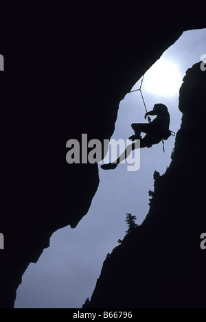 Silhouette de rock climber hanging from falaise Banque D'Images