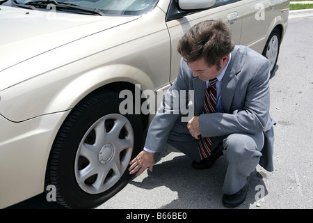 Un homme habillé pour une réunion d'affaires à la découverte d'un pneu à plat sur sa voiture Banque D'Images