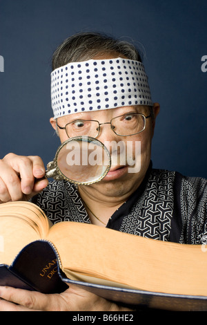 Japonais Senior homme portant un costume traditionnel utilise une loupe pour lire un dictionnaire Banque D'Images